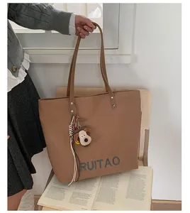 Détail d'un sac cabas marron avec broderie de lettres et breloque chien en peluche