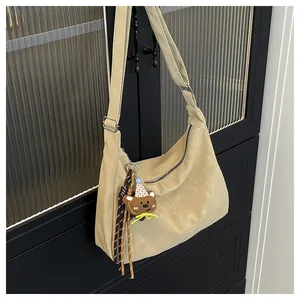 Detail of beige half-moon shoulder bag with cute bear charm on frosted texture material