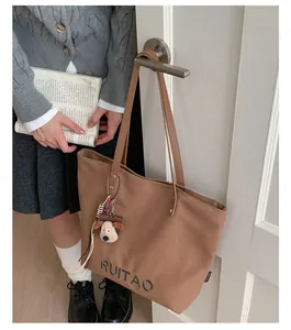 Détail du sac cabas en toile marron avec broderie de lettres et pendentif chiot
