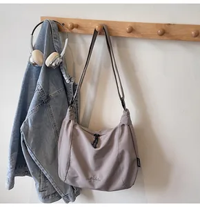 Detail of gray half-moon crossbody bag with Midolee logo hanging on a wooden hook