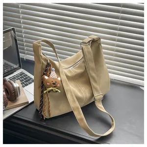 Detail of minimalist beige PU leather crossbody bag featuring a cute teddy bear charm