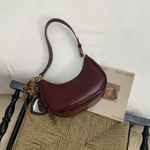 Détail du sac demi-lune bordeaux avec accent léopard et breloque en forme de pompon doux