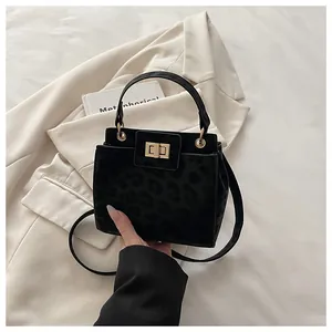 Détail du sac à main noir léopard avec fermoir rotatif doré posé sur un blazer ivoire