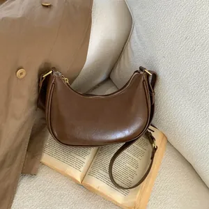 Détail d'un sac hobo en cuir marron avec garniture dorée posé sur un livre ouvert