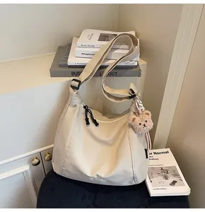 Detail of off-white canvas crossbody bag with teddy bear charm and adjustable strap