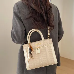 Détail d'un sac à bandoulière tissé beige avec finitions en cuir crème et breloque perlée