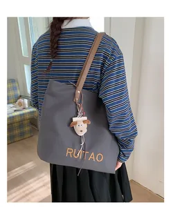 Détail du sac cabas en toile grise avec bandoulière en cuir et breloque mouton
