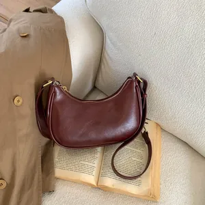 Détail d'un sac demi-lune bordeaux avec finitions dorées posé sur un livre ancien
