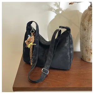 Close-up of black matte crossbody bag with a cute bear charm on a wooden cabinet