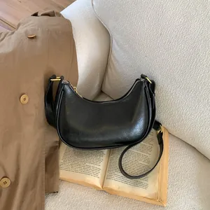 Détail du sac hobo croissant en cuir noir avec ferrures dorées sur un canapé