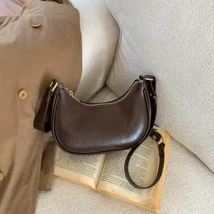 Gros plan du sac demi-lune marron foncé en cuir mat lisse avec détails dorés brillants