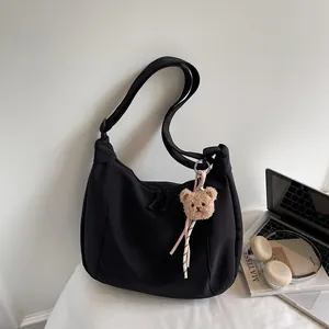 Minimalist black nylon tote bag with teddy bear charm shown in a creative lifestyle setting
