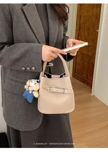 Close-up of beige grained leather bucket bag with a cute bear charm and metal buckle