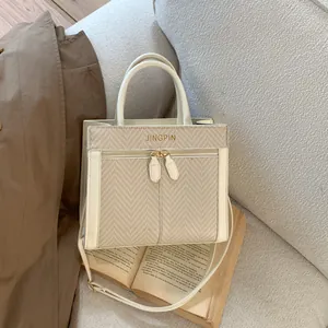 Détail du sac bandoulière crème avec texture tissée et logo doré sur un canapé gris