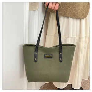 Detail of olive green corduroy tote bag featuring leather straps and golden rivets