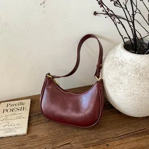 Détail du sac demi-lune bordeaux sur une table en bois avec décor élégant