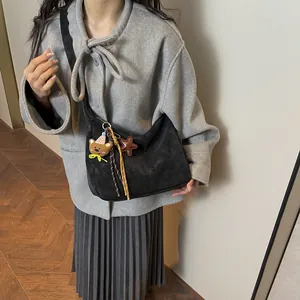 Minimalist black vintage messenger bag with bear charm shown on a stylish model