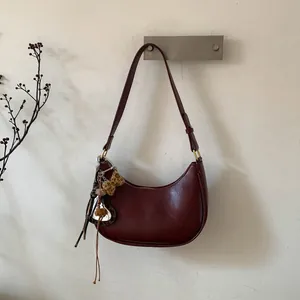 Détail du sac hobo croissant bordeaux avec nœud léopard et charm cœur sur mur épuré