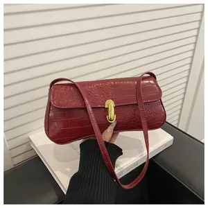 Detail of burgundy crocodile pattern handbag with glossy finish and gold metal buckle
