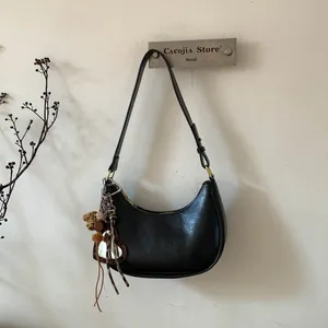 Détail du sac croissant noir avec breloque cœur léopard et accessoires à pompons