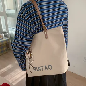 Détail d'un sac cabas en toile avec broderie, lanières en cuir et breloque peluche