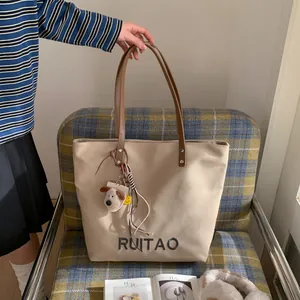 Détail du cabas en toile beige avec anses en cuir marron et breloque chien peluche