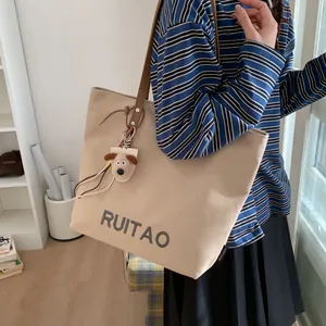 Gros plan d'un sac cabas en toile beige avec broderie grise et breloque chien peluche
