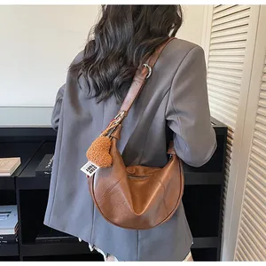 Détail d'un sac demi-lune marron avec breloque cœur en peluche et bandoulière