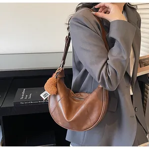 Sac demi-lune marron avec breloque cœur et sangle tissée porté sur un blazer gris