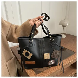 Detail shot of black faux leather tote with decorative fashion patches and dual handles