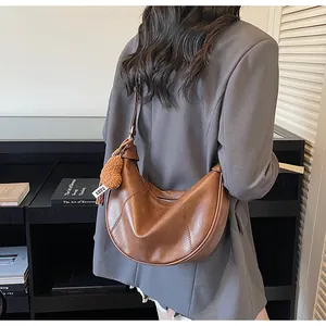 Détail d'un sac demi-lune en cuir marron avec charm en peluche cœur et fermeture éclair