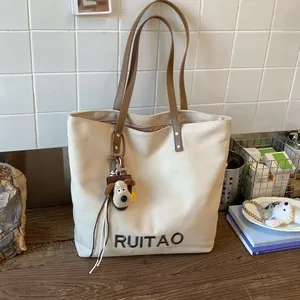Vue détaillée du sac cabas en toile avec broderie de lettres et breloque chiot en peluche