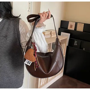 Détail d'un sac demi-lune marron foncé avec pendentif coeur et coutures contrastées