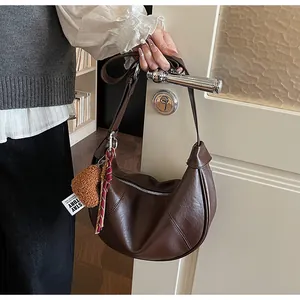 Détail d'un sac demi-lune marron foncé avec charme cœur suspendu à une poignée