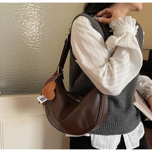 Détail du sac croissant en cuir marron foncé avec breloque ours et ruban élégant