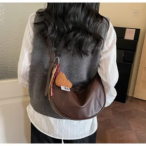 Détail du sac croissant marron foncé avec pendentif cœur en peluche et nœud tressé