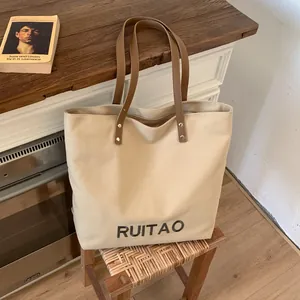 Détail du sac cabas en toile beige avec broderie RUITAO et poignée en cuir à rivets
