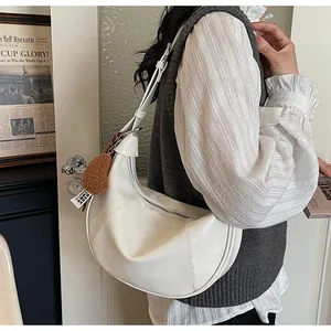 Détail d'un sac demi-lune crème avec pendentif cœur en peluche et bandoulière