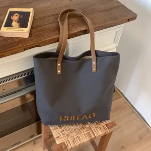 Détail du sac cabas en toile gris foncé avec anses en cuir marron et broderie RUITAO