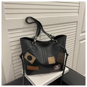 Detail of black leather tote bag with colorful patches and gold rivet hardware accents