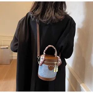 Detail of blue denim bucket bag with brown leather trim and silk scarf wrapped handle