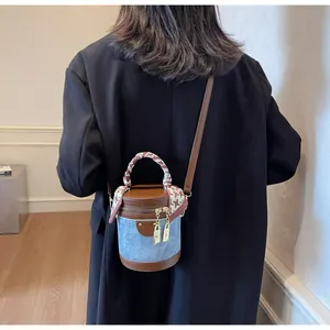 Detail of blue denim bucket bag with brown leather trim and houndstooth scarf handle