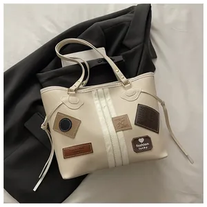 Close-up of beige tote bag featuring vintage leather badges and vertical stripe details