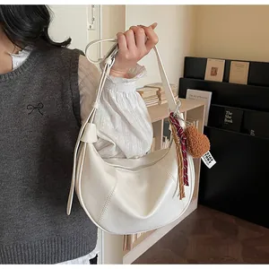 Détail d'un sac demi-lune beige avec coutures et pendentif en peluche sur la bandoulière