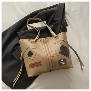 Detailed close-up of light brown tote bag with vintage patches and side fringe tassels