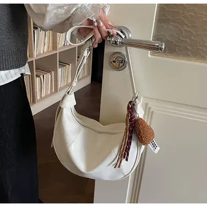 Sac à bandoulière en croissant blanc avec gland rouge foncé et pompon marron sur une poignée