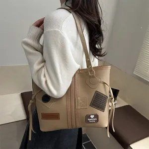 Khaki large capacity PU tote bag with vintage patches and drawstring, shown on shoulder