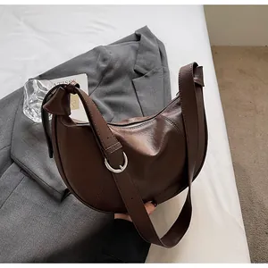 Détail du sac croissant marron foncé avec boucle argentée sur fond gris élégant