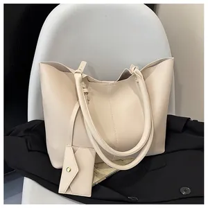 Close-up of beige PU leather tote bag with matching envelope pouch on a black suit