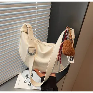 Détail du sac croissant blanc cassé avec un pendentif ours en peluche et boucle argentée